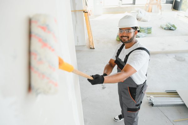 An Indian apartment repair worker paints a white wall with a roller.