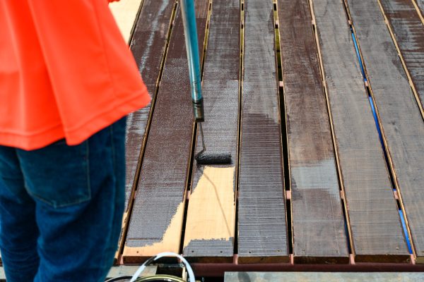 Worker painting with paint roller on wooden floor